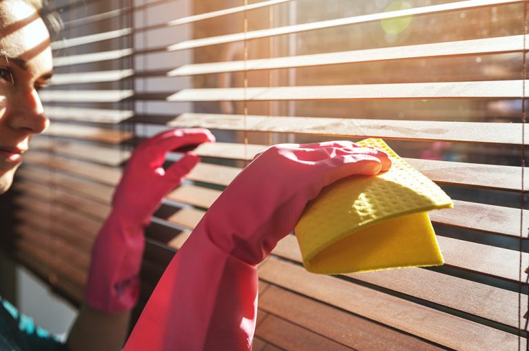 Frau reinigt zu Hause hölzerne Jalousien von Staub.